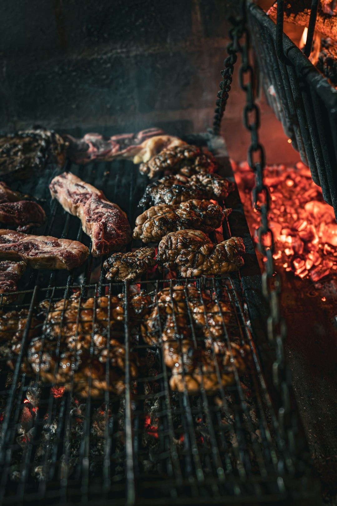 Raw steak and sweetbreads cooking on a grill over hot charcoal.
